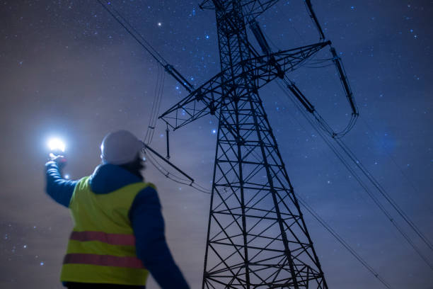 Electricity engineer working on Electrical Pylons Translation, checking the condition of the Electrical Power Pole components at night.